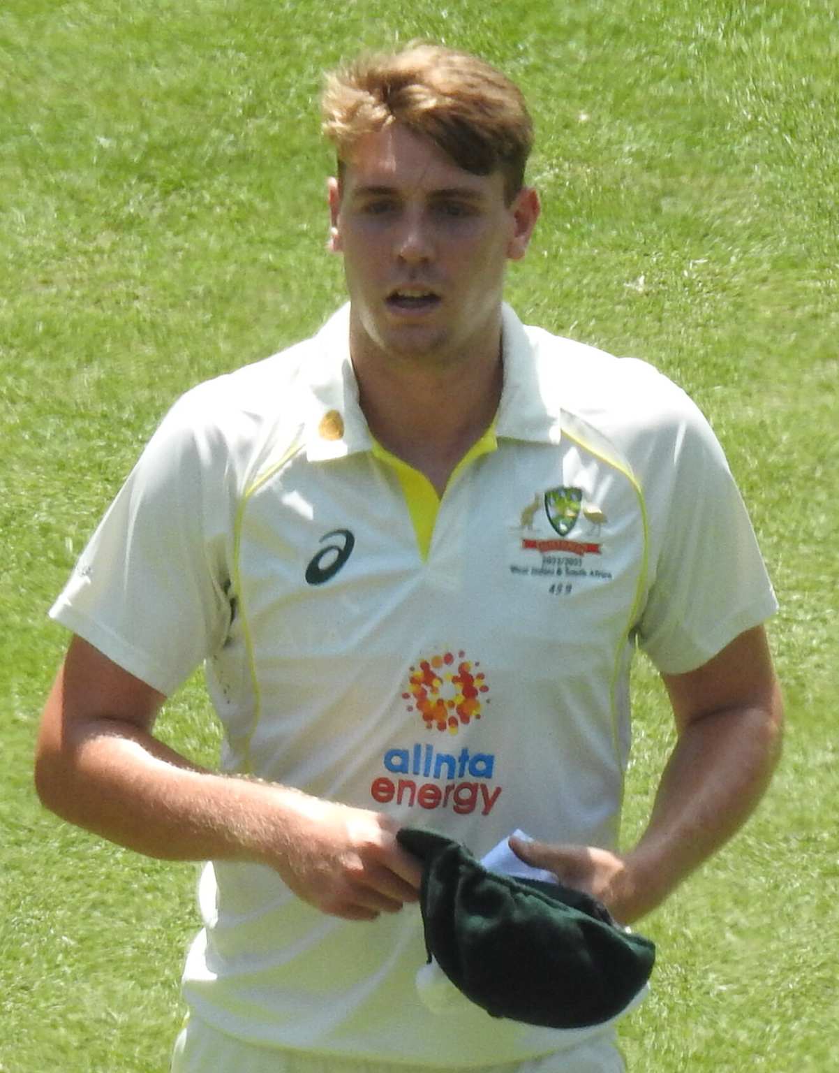 Australian cricket player wearing team jersey holding a cricket cap on the field
